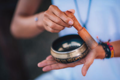 Midsection of woman holding singing bowl while doing yoga at lake