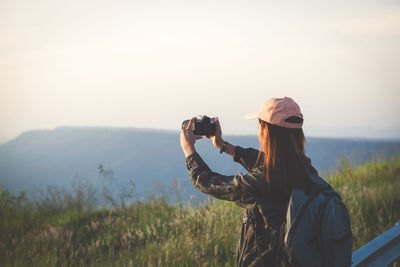 Woman photographing on field against clear sky