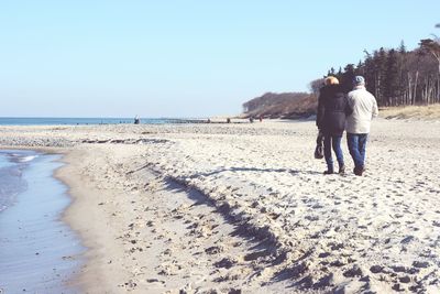 Rear view of people walking on shore at beach against sky