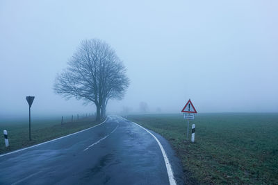Road amidst field against sky during foggy weather