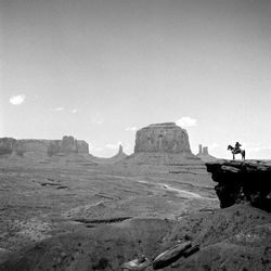 Man riding horse by rock formation against sky