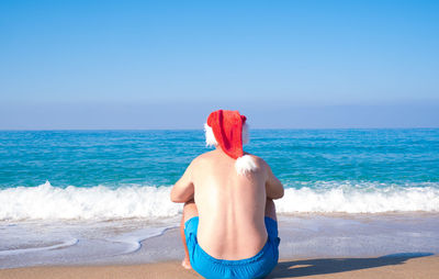 A man in a santa claus hat sits on the seashore, rear view. christmas santa claus relaxing