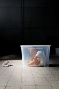 Doll in plastic container on tiled floor at home