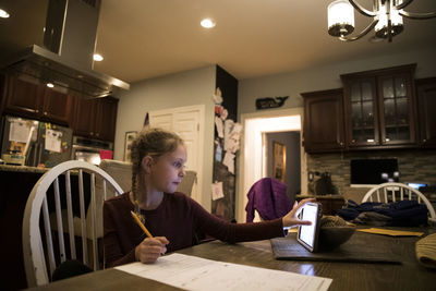 Blonde girl at kitchen table does school work on tablet computer