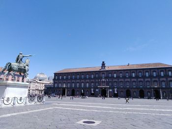 People in historic building against clear blue sky