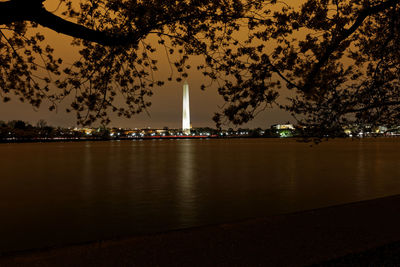 Illuminated city by river against sky at night