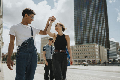 Fashionable young man dancing with female friend while walking on street in city