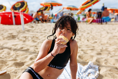 Sitting on the sand beach girl with wet hair eating the bread