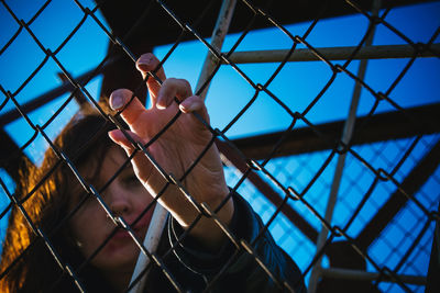 Woman holding chainlink fence against clear blue sky
