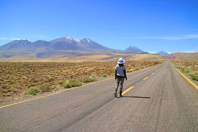 Rear view of woman walking on empty road against sky