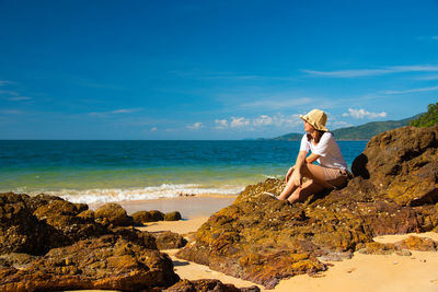Woman sitting on rock at beach against sky