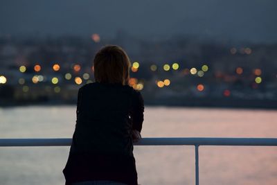 Rear view of woman looking at illuminated city by river at night