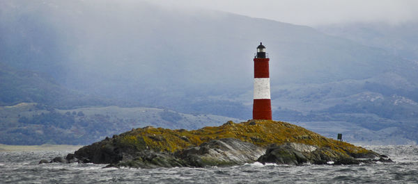 Lighthouse on cliff by sea against sky