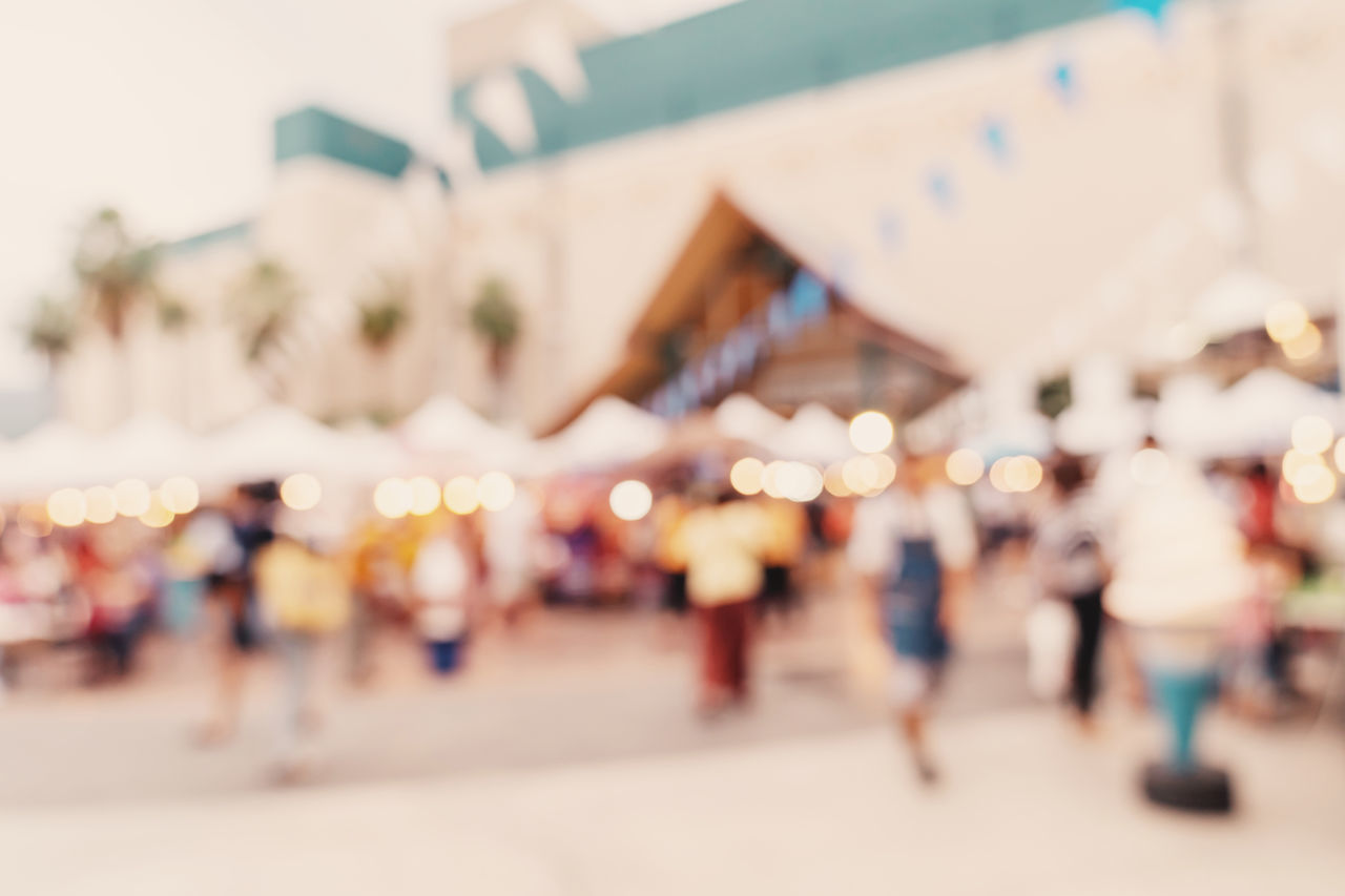 DEFOCUSED IMAGE OF CROWD WALKING ON ILLUMINATED STREET