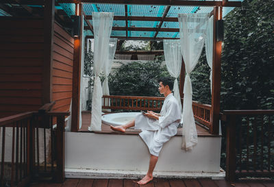 Young man wearing bathrobe sitting by hot tub