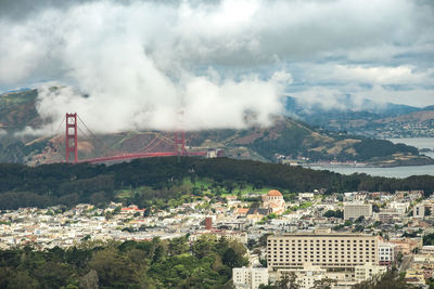 Cityscape by golden gate bridge against cloudy sky