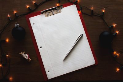 High angle view of illuminated string light by lined paper on clipboard at table