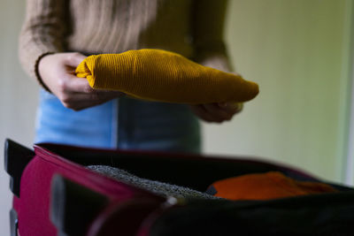 Traveler woman keeping a yellow pullover in the travel suitcase.