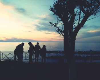 Silhouette people standing by sea against sky during sunset