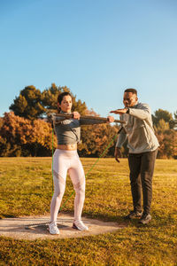 Woman pulling belt while instructor guiding on land against clear sky