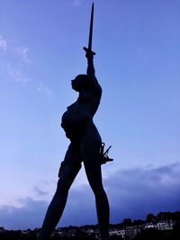 Low angle view of silhouette statue against blue sky