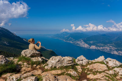 Rear view of man sitting on rock against sky