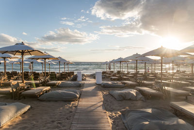 Parasols with seats arranged at beach against sky during sunset
