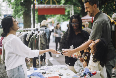 Side view of happy female vendor laughing while taking online payment from customer at flea market