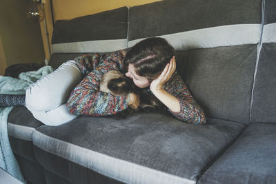 Woman kissing cat while lying on sofa