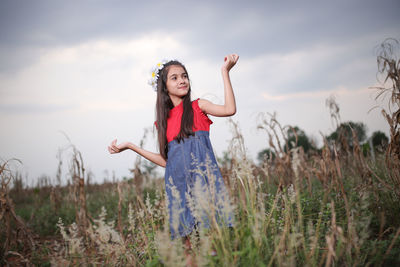 Smiling cute girl standing amidst plants on field during sunset