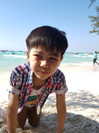 Boy looking away while kneeling on beach against clear sky