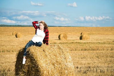 Full length of woman sitting on bale against sky