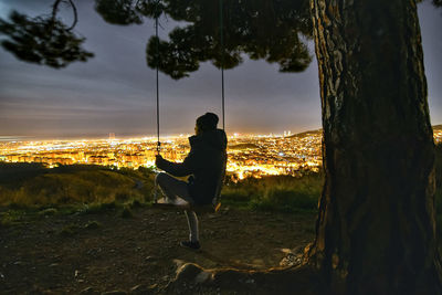 Rear view of man sitting on tree trunk against sky