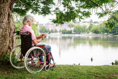 Woman sitting on bench by lake against trees