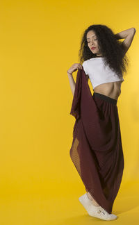 Young woman standing against yellow background