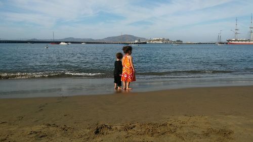 Rear view of sisters standing on shore at beach