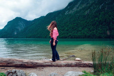 Rear view of woman standing by lake against mountains