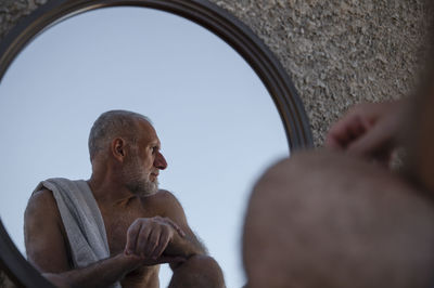 Shirtless adult man looking away in mirror