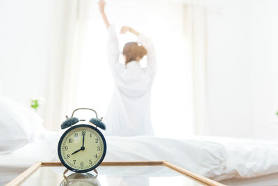 Alarm clock on table with woman in background at home