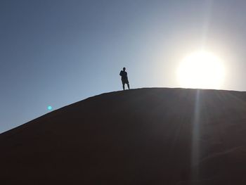 Low angle view of silhouette man standing on mountain against sky during sunny day