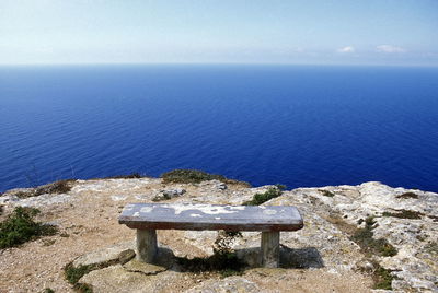 Stone bench on rock formation against blue sea