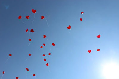 Low angle view of heart shape balloons flying against blue sky