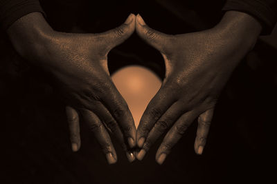 Close-up of cropped hands amidst egg against black background