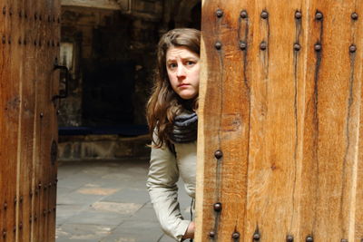 Portrait of scared woman standing by wooden door