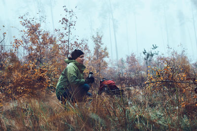 Woman with backpack having break during autumn trip drinking a hot drink from thermos flask