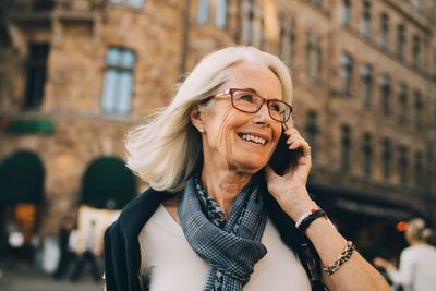 Smiling wrinkled woman talking through phone while looking away in city