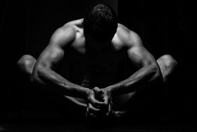 Shirtless man sitting against black background