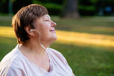 Portrait of relaxed senior plus size woman with earphones with closed eyes outdoors enjoying music