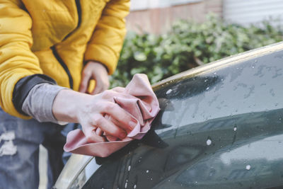 A young man wipes the headlights of a car with a rag.