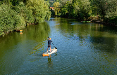 Rear view of man paddling on sup board on river.